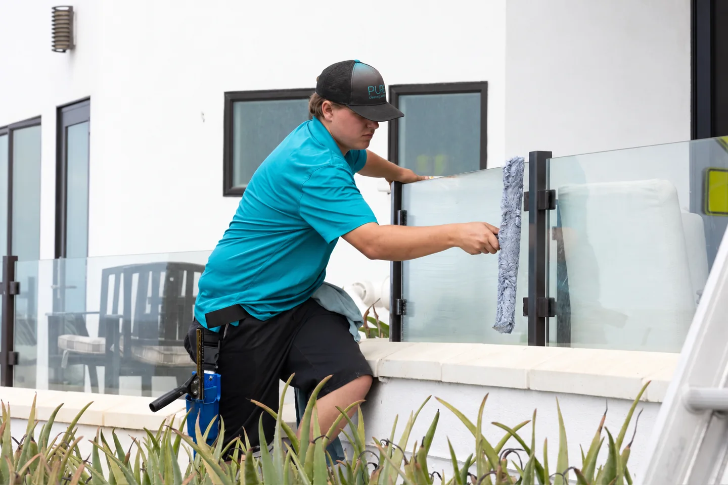 PCS technician carefully washing a glass railing beside a patio