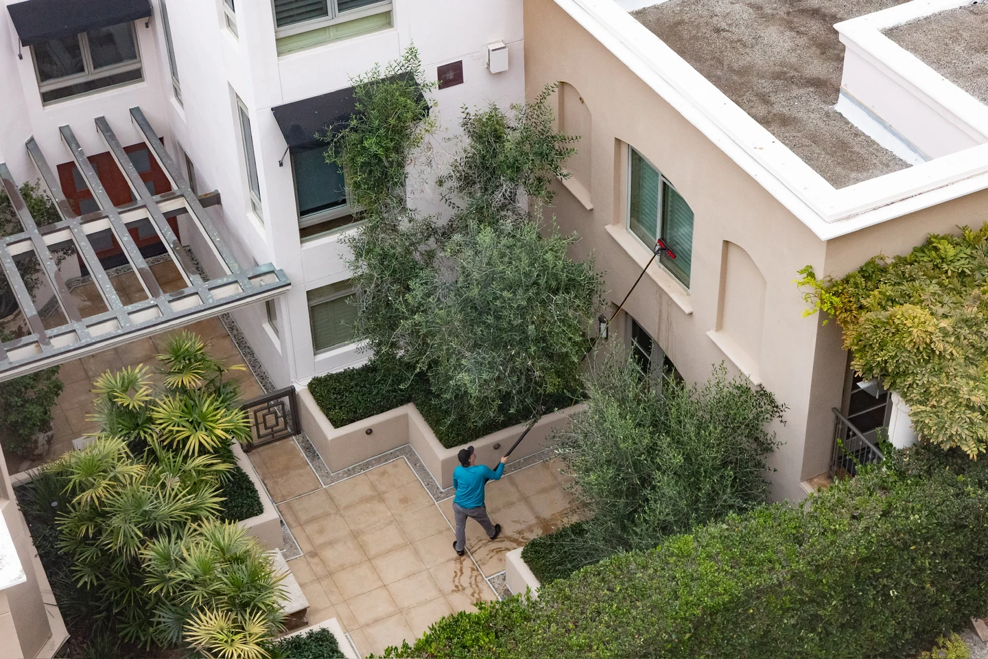 PCS technician cleaning upper courtyard windows with an extension pole at a residential community